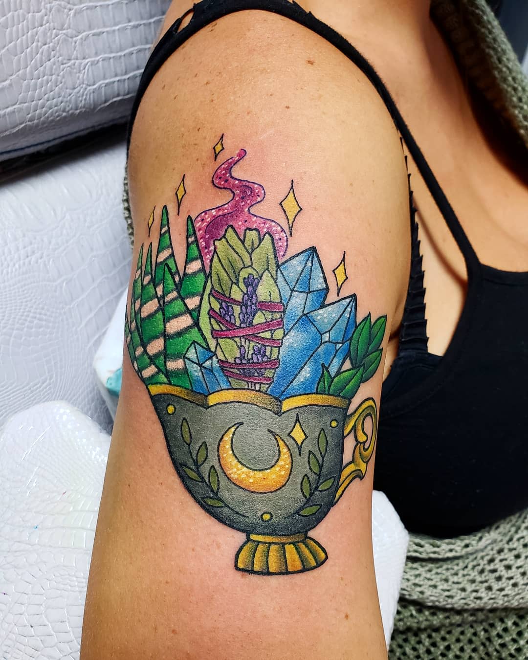 Tattoo on upper arm of a teacup with crystals, succulents, and a swirl of pink smoke decorated with stars